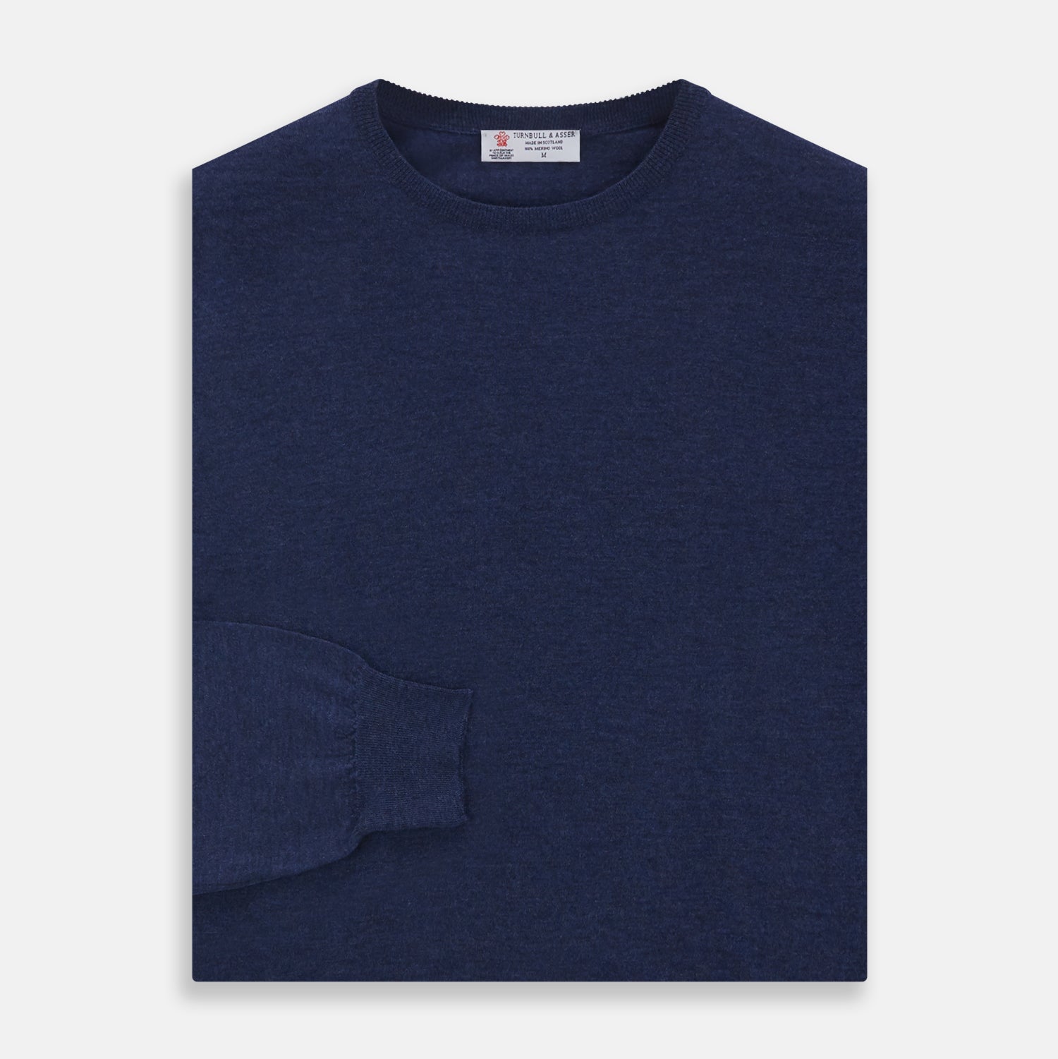 View 3 of product The Blue Crew Neck Merino Wool Jumper by Turnbull & Asser—a classic, long-sleeved staple with ribbed cuffs and hem—lies flat against a white background.