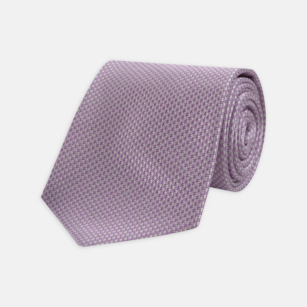 The Turnbull & Asser Lilac Houndstooth Silk Tie features a subtle houndstooth pattern and elegant silk weave—ideal for elevating your favorite office shirt. Displayed rolled on a white background.