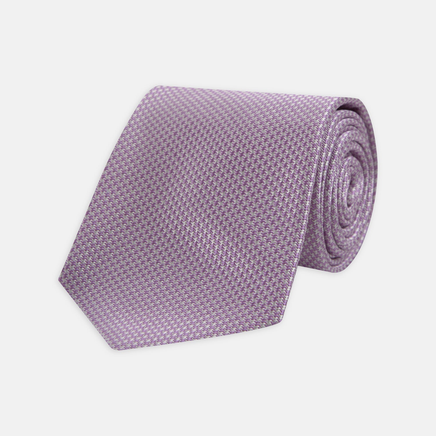 View 1 of product The Turnbull & Asser Lilac Houndstooth Silk Tie features a subtle houndstooth pattern and elegant silk weave—ideal for elevating your favorite office shirt. Displayed rolled on a white background.