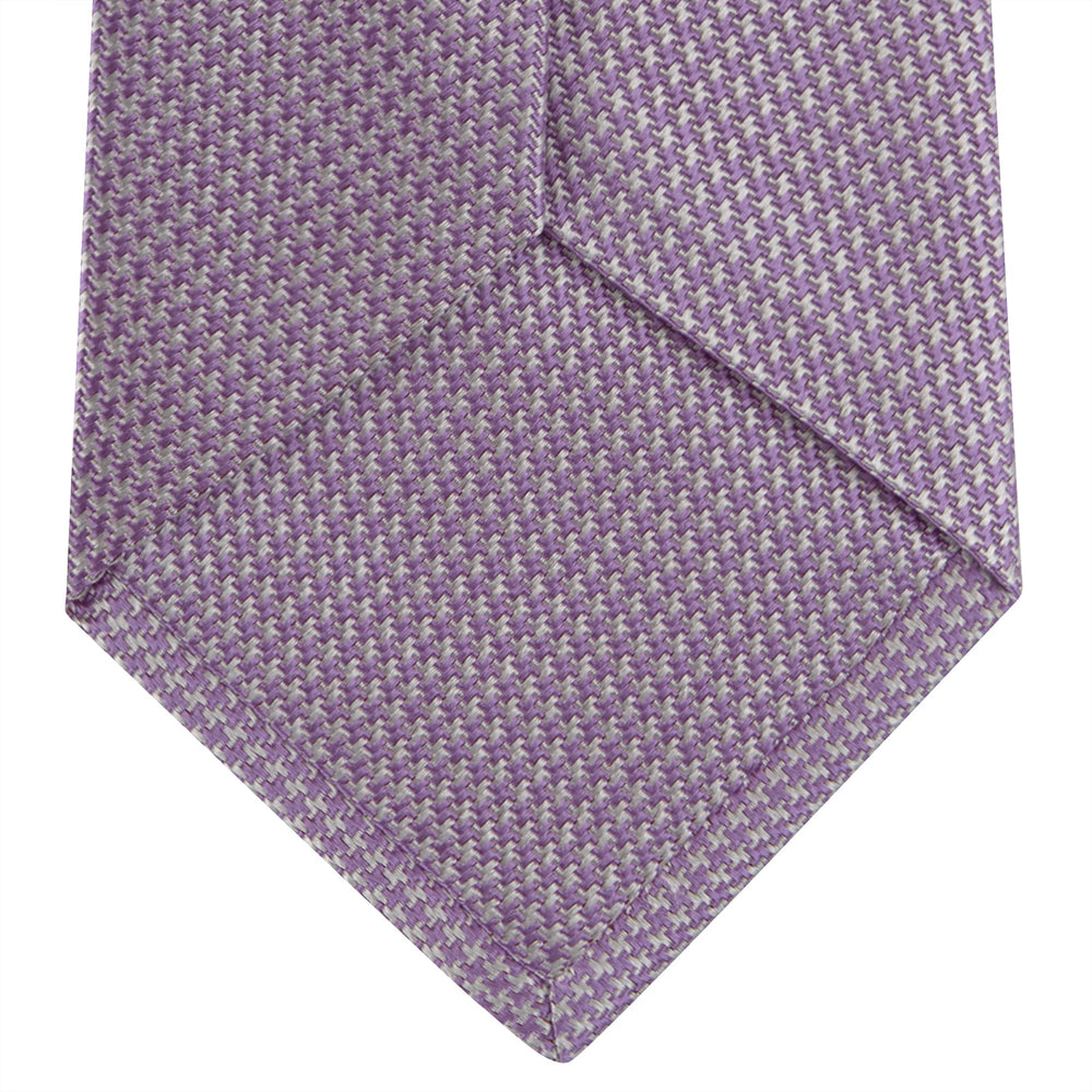 The Turnbull & Asser Lilac Houndstooth Silk Tie features a subtle houndstooth pattern and elegant silk weave—ideal for elevating your favorite office shirt. Displayed rolled on a white background.