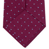 View 4 of product The Turnbull & Asser Dark Pink and Blue Spot Lace Silk Tie features small, evenly spaced blue dots on dark pink silk, shown rolled up against a white background.