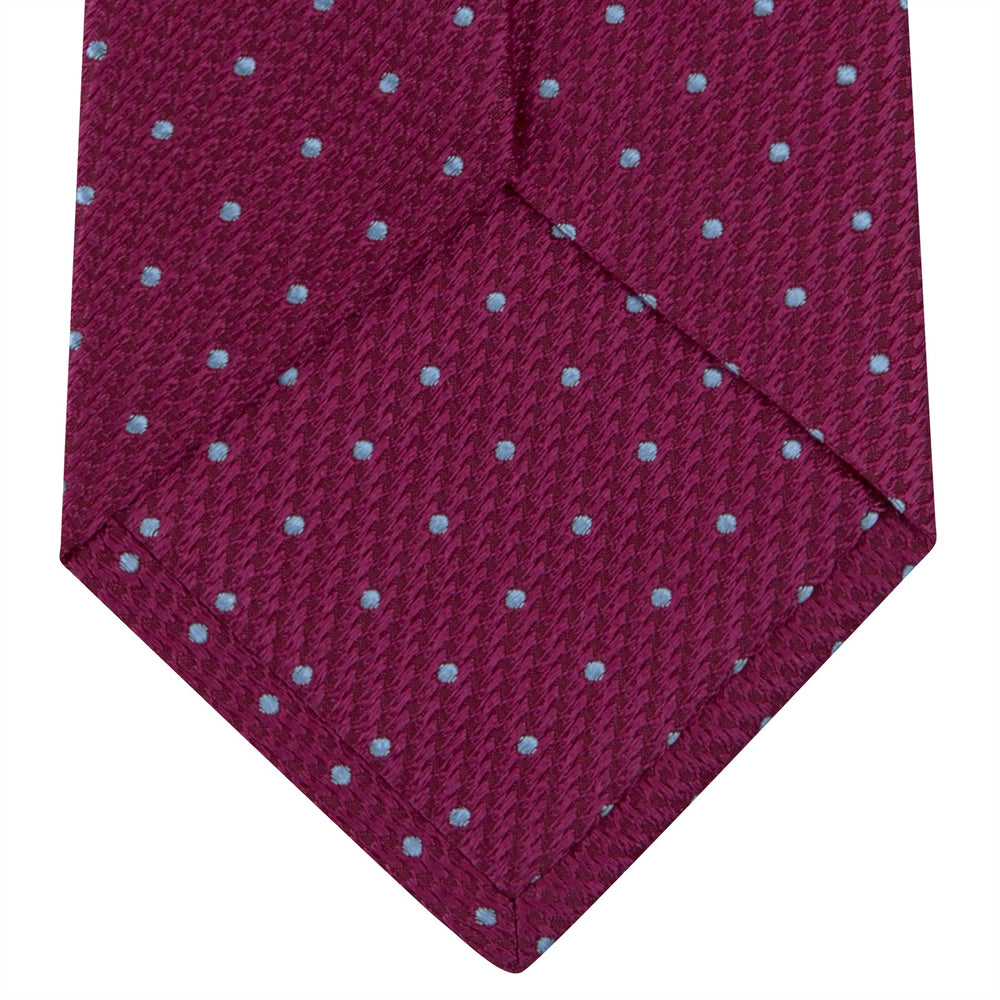 The Turnbull & Asser Dark Pink and Blue Spot Lace Silk Tie features small, evenly spaced blue dots on dark pink silk, shown rolled up against a white background.