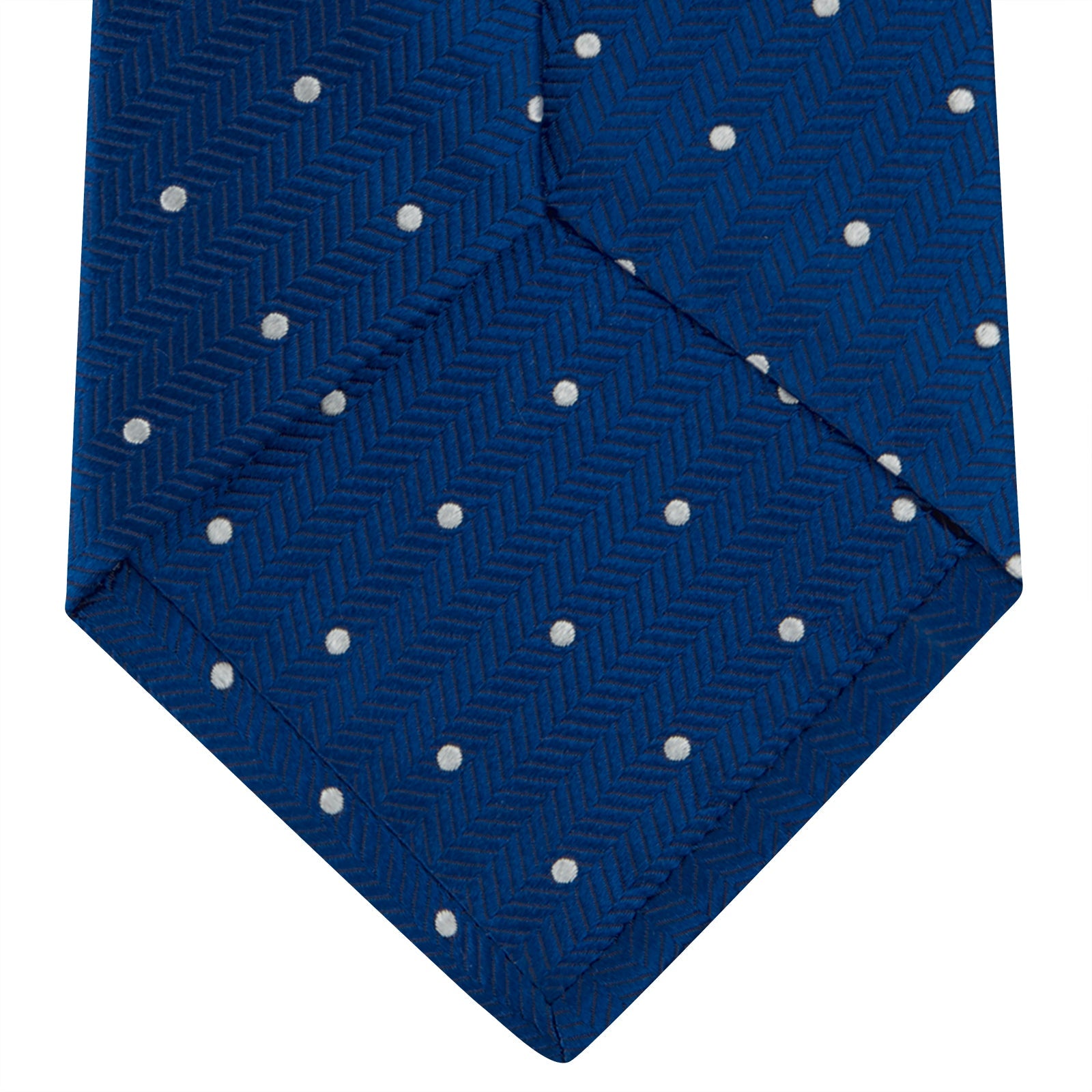 View 4 of product The Turnbull & Asser Royal Blue and White Small Spot Herringbone Silk Tie is displayed rolled at one end on a plain white background, showcasing its classic English silk design with subtle white polka dots.