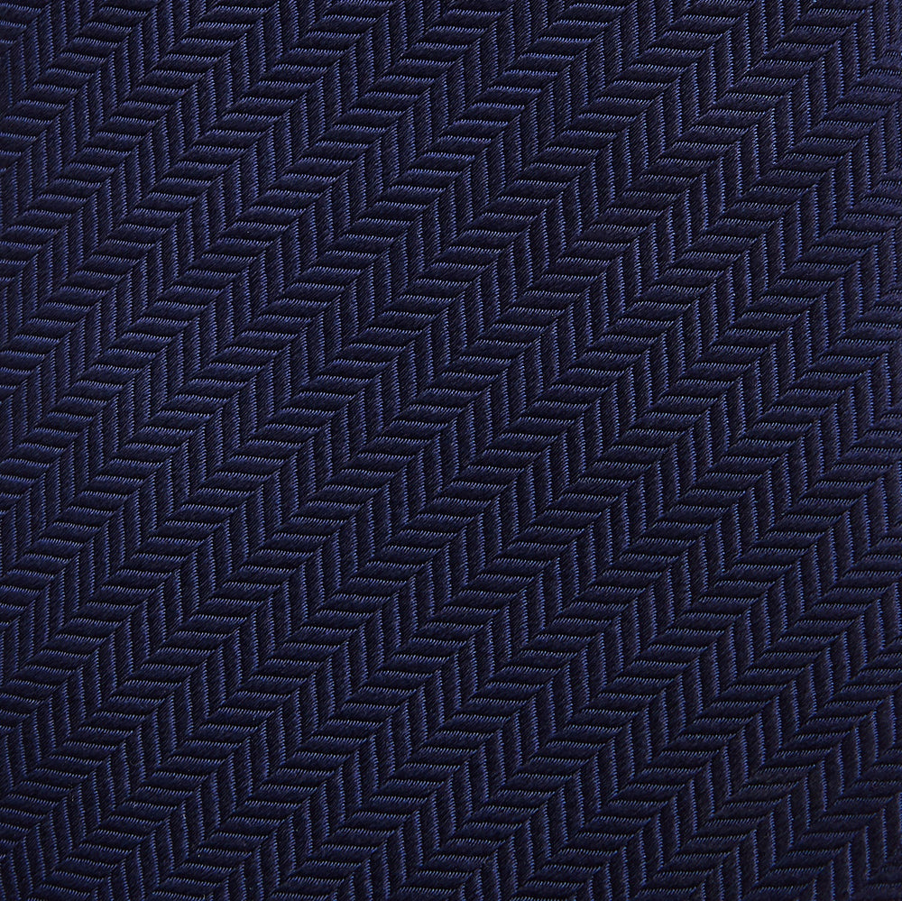The Turnbull & Asser Slim Navy Herringbone Silk Tie is a refined men’s accessory, elegantly rolled and displayed on a plain white background.
