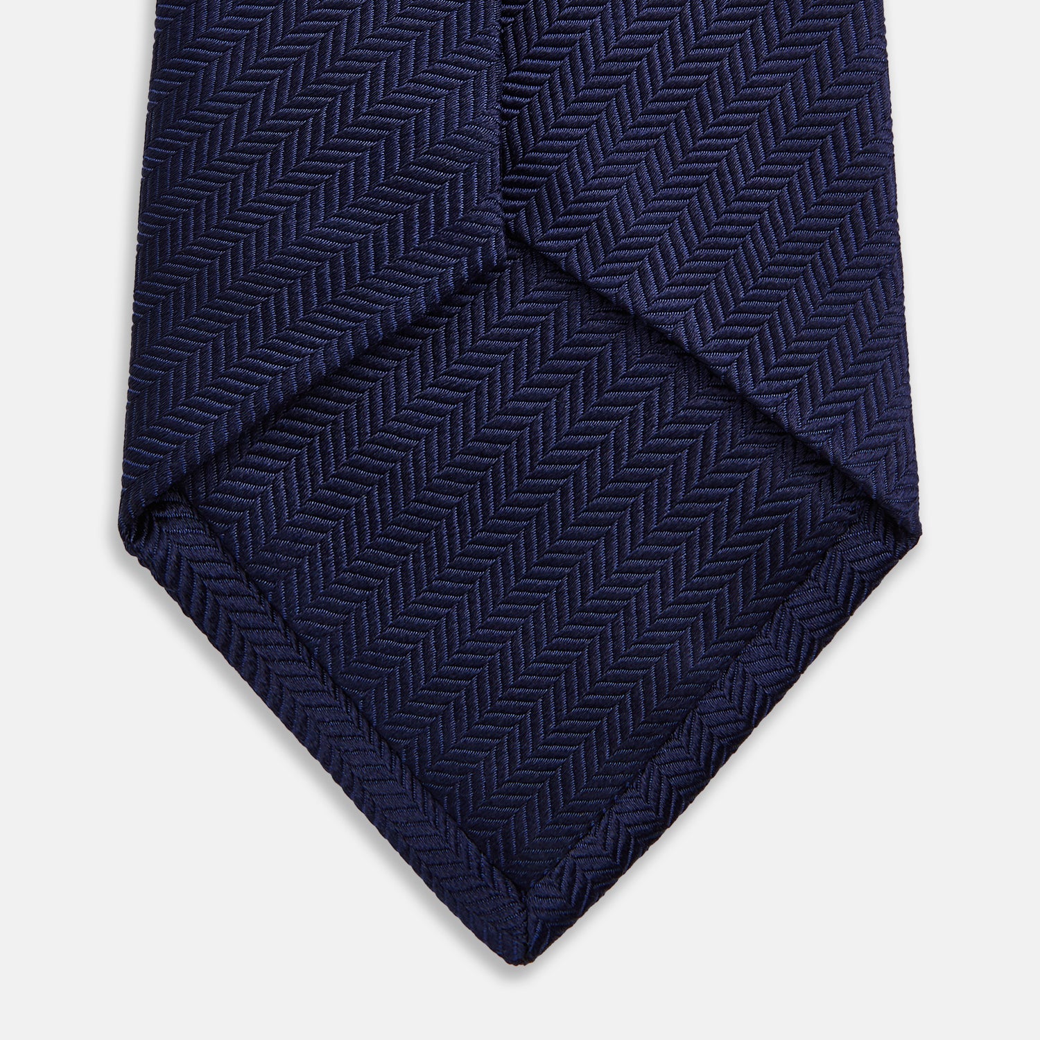 View 4 of product The Turnbull & Asser Slim Navy Herringbone Silk Tie is a refined men’s accessory, elegantly rolled and displayed on a plain white background.