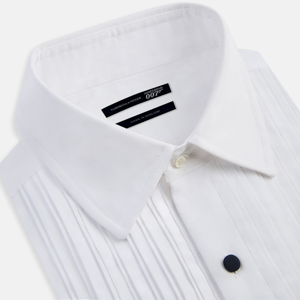 The Casino Royale White Dress Shirt in Cotton by Turnbull & Asser UK is a long-sleeve white dress shirt, crafted from crisp white cotton poplin with a pleated bib front, black buttons, and a classic collar, shown laid flat on a white background.