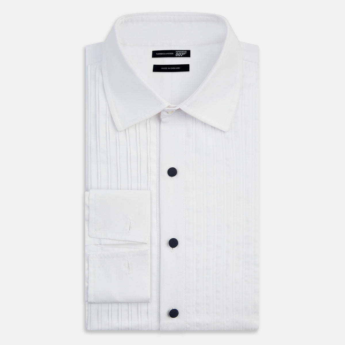 View 5 of product The Casino Royale White Dress Shirt in Cotton by Turnbull & Asser UK is a long-sleeve white dress shirt, crafted from crisp white cotton poplin with a pleated bib front, black buttons, and a classic collar, shown laid flat on a white background.
