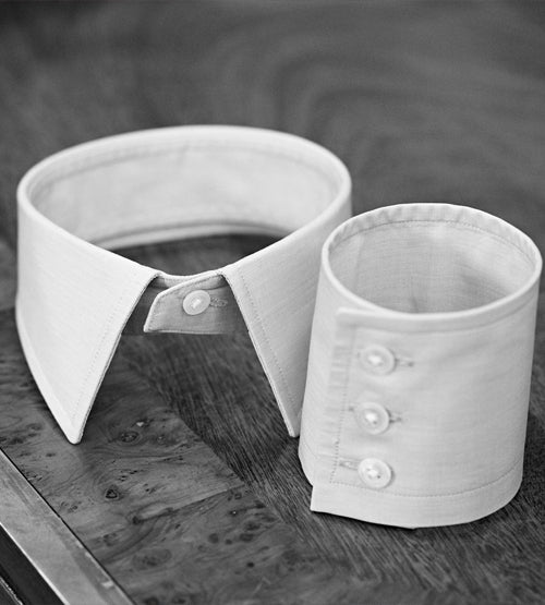 A detachable white shirt collar and a matching shirt cuff with three buttons are displayed on a wooden surface.