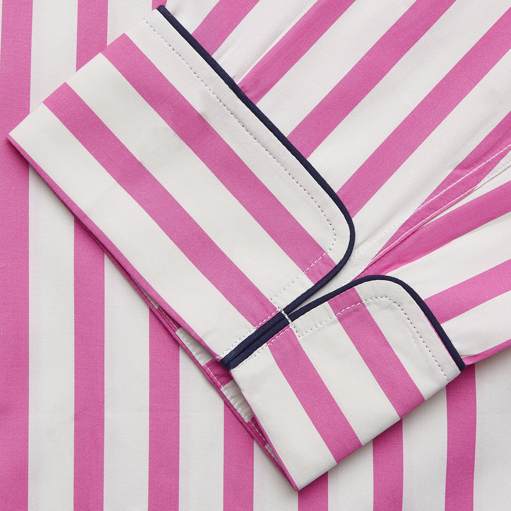 The Turnbull & Asser Pink Candy Stripe Cotton Traditional Pyjamas feature long sleeves, pants, vertical pink candy stripes, a camp collar shirt with buttons, chest pocket, and navy trim on the pocket and cuffs.