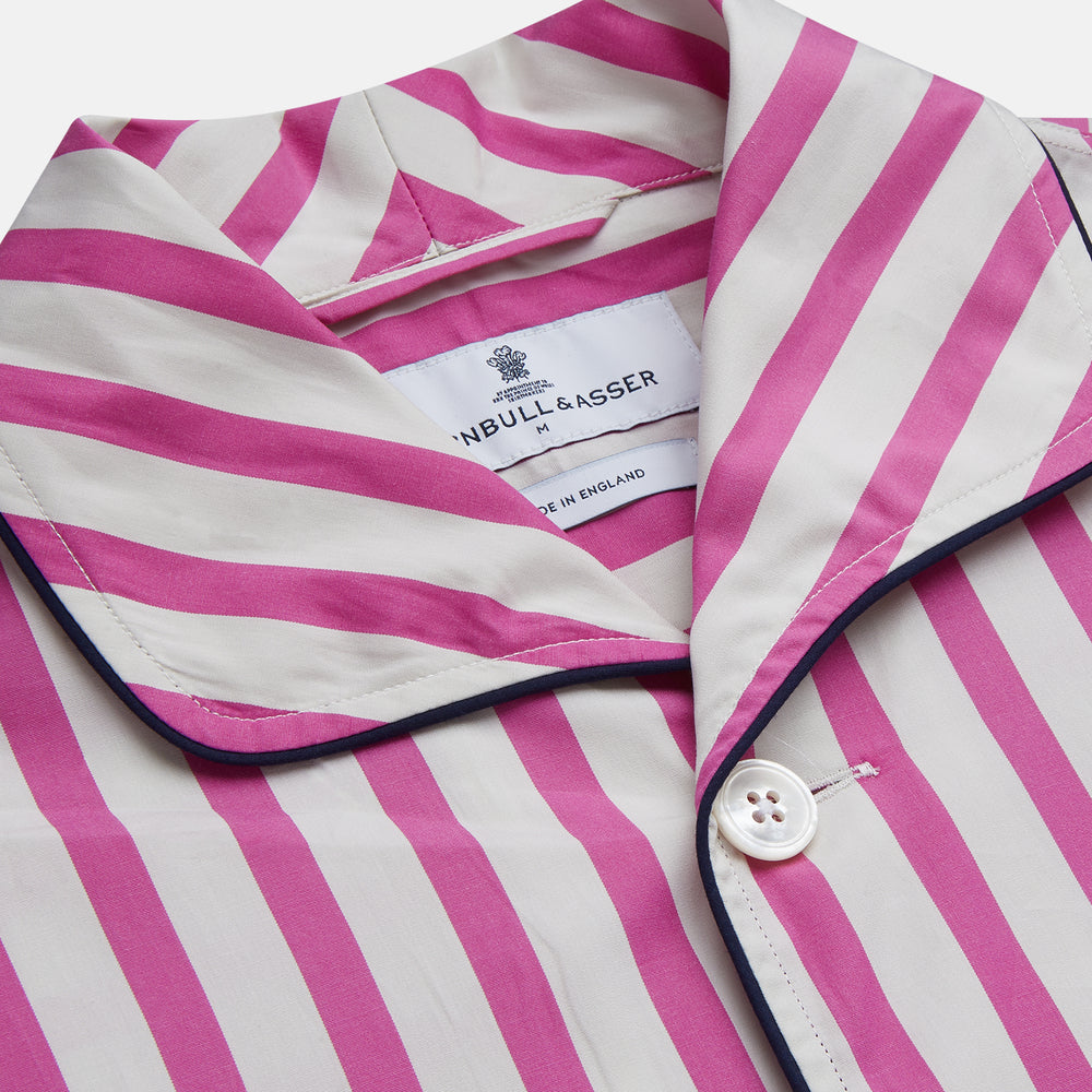 The Turnbull & Asser Pink Candy Stripe Cotton Traditional Pyjamas feature long sleeves, pants, vertical pink candy stripes, a camp collar shirt with buttons, chest pocket, and navy trim on the pocket and cuffs.