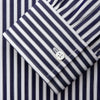 View 4 of product A person in a Turnbull & Asser Navy & White Stripe Weekend Fit Shirt with Derby Collar and Single Button Cuffs, paired with a paisley tie and dark pants, stands indoors leaning against a cream paneled wall.