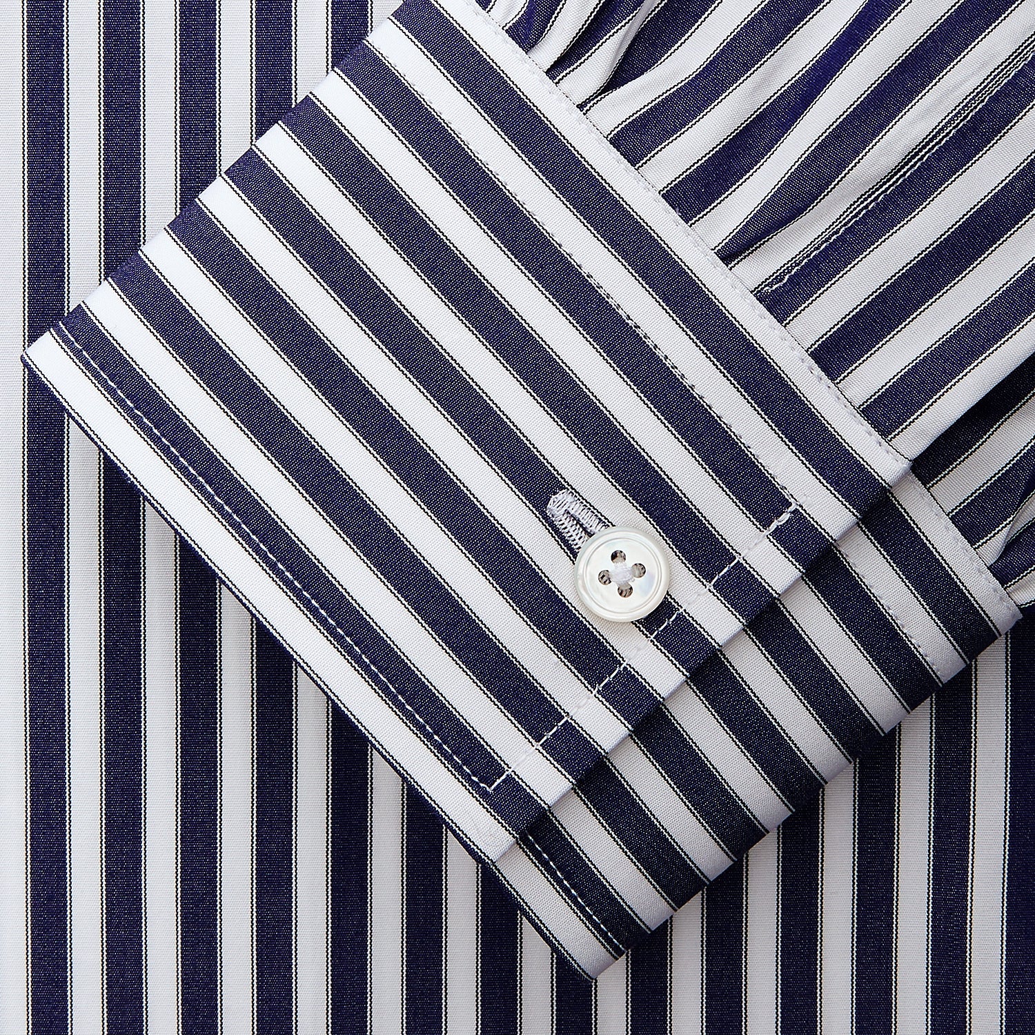 View 4 of product A person in a Turnbull & Asser Navy & White Stripe Weekend Fit Shirt with Derby Collar and Single Button Cuffs, paired with a paisley tie and dark pants, stands indoors leaning against a cream paneled wall.