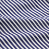 View 5 of product A person in a Turnbull & Asser Navy & White Stripe Weekend Fit Shirt with Derby Collar and Single Button Cuffs, paired with a paisley tie and dark pants, stands indoors leaning against a cream paneled wall.