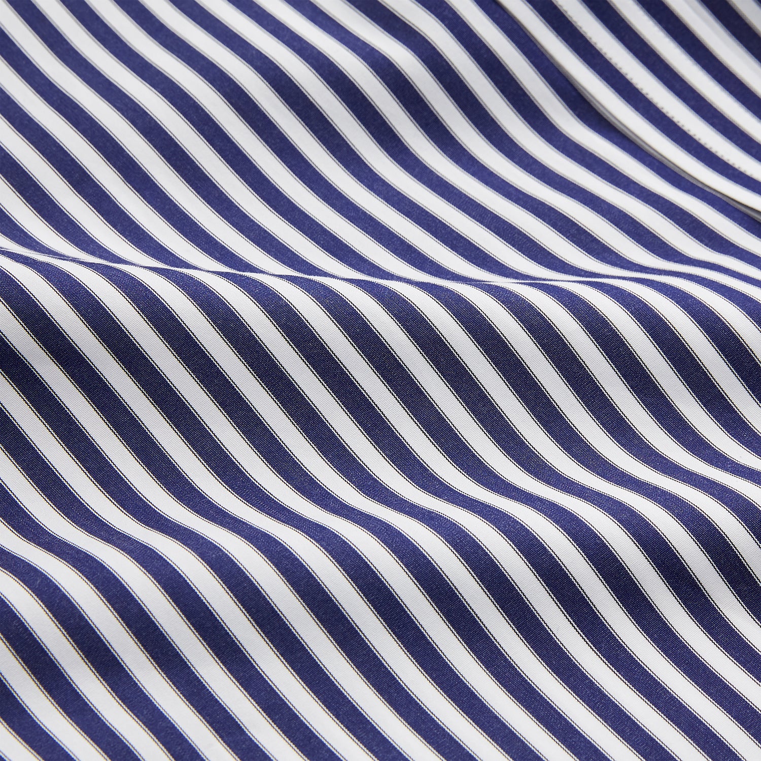 View 5 of product A person in a Turnbull & Asser Navy & White Stripe Weekend Fit Shirt with Derby Collar and Single Button Cuffs, paired with a paisley tie and dark pants, stands indoors leaning against a cream paneled wall.