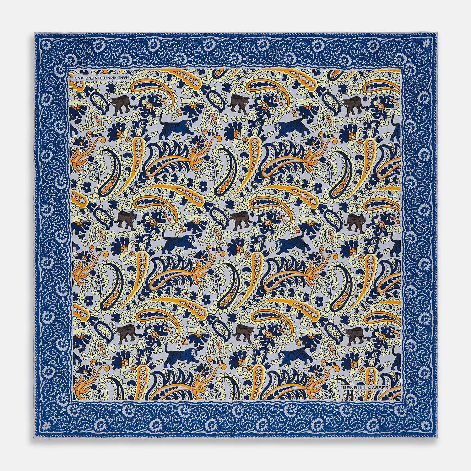View 1 of product The Blue and Yellow Paisley Tiger Silk Pocket Square by Turnbull & Asser features a light blue base with paisley, elephants, tigers, and floral motifs—highlighted by a blue border. An elegant choice to pair with any Turnbull shirt.