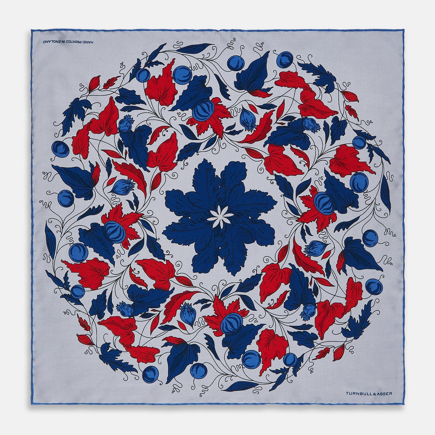 View 1 of product The Blue and Red Foliage Pattern Silk Pocket Square by Turnbull & Asser features intricate symmetrical leaves and flowers in red, blue, and navy on a light grey silk background, creating an elegant circular motif.