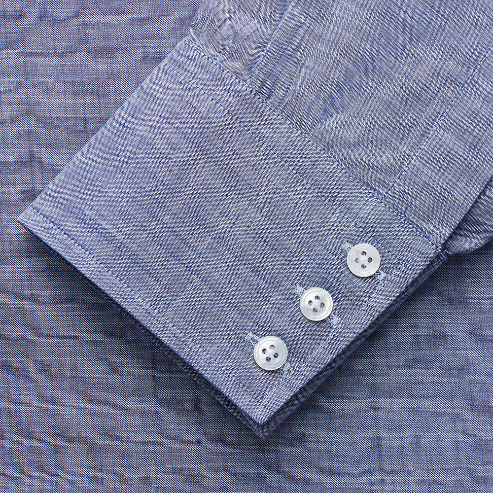 The Turnbull & Asser Blue Chambray Cotton Regular Fit Mayfair Shirt features a subtle textured pattern, pointed T&A collar, and white buttons. Shown here in a light blue shade, laid flat on a white background.