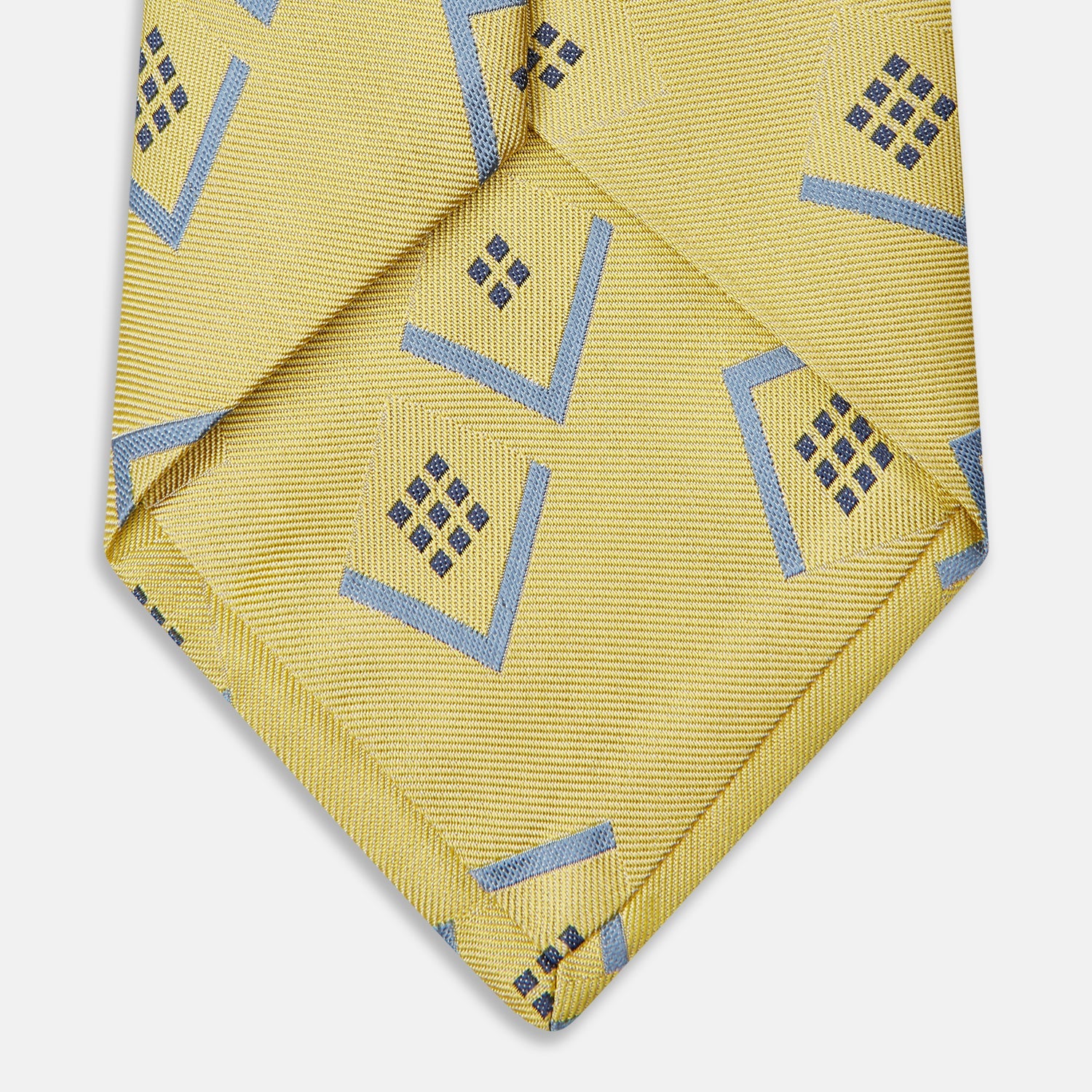 View 3 of product The Turnbull & Asser Yellow Graphic Deco Silk Tie features a subtle pattern of light blue geometric shapes and small black dots, elegantly rolled against a white background.