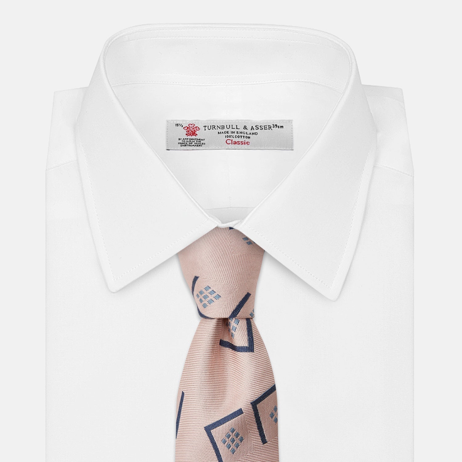 View 3 of product The Turnbull & Asser Pink Graphic Deco Silk Tie features blue geometric and square patterns on pale pink silk, shown rolled with the pointed end facing forward.