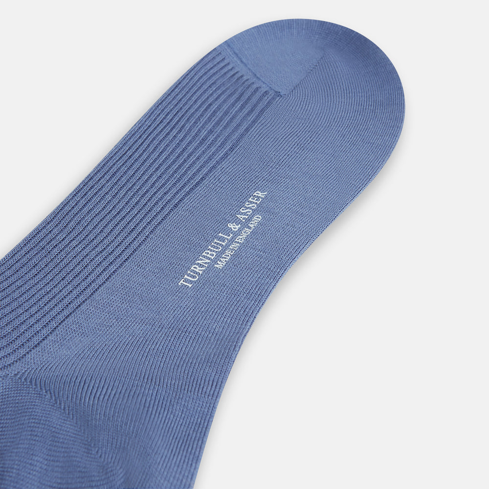 A single Powder Blue Mid-Length Merino Sock by Turnbull & Asser stands upright against a white background, showcasing its smooth texture and subtle vertical lines, with a length that reaches just below the knee.