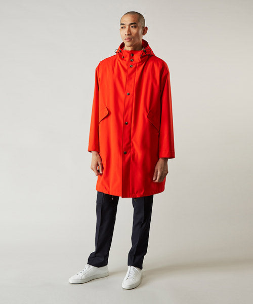 A person stands against a plain background wearing a bright red hooded raincoat, black pants, and white sneakers.