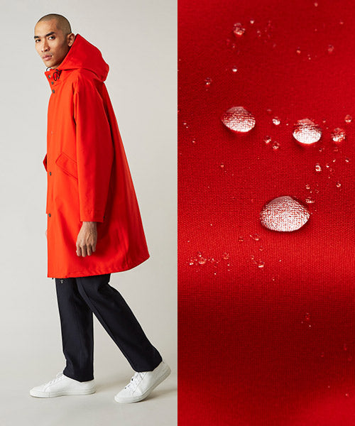 A person wearing a bright red hooded raincoat, dark pants, and white sneakers stands next to a close-up of water droplets beading on red fabric, highlighting its waterproof quality.