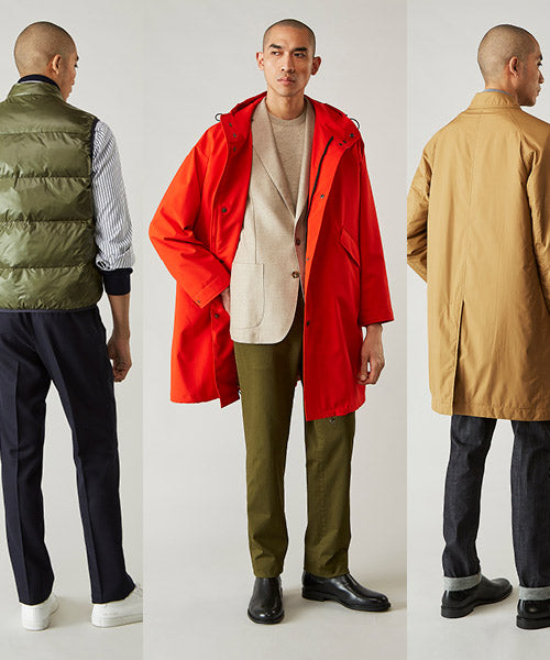 Three men modeling fall outfits: left wears a green puffer vest, striped shirt, and navy trousers; center wears a bright red coat over a beige blazer and green pants; right wears a tan coat with dark pants and black shoes.
