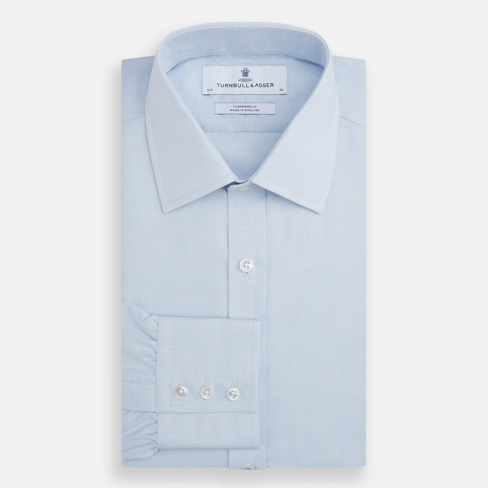 The Turnbull & Asser Blue Cashmerello Mayfair Shirt is a light blue cotton-cashmere blend with long sleeves, pointed collar, white buttons, and buttoned cuffs, shown on a plain white background.
