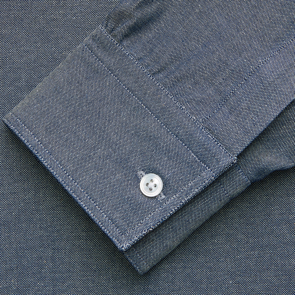 The Turnbull & Asser Blue Chambray Weekend Fit Nevis Cotton Shirt features a Dorset collar, 1-button cuffs, and smart-casual tailoring, shown laid flat on a white background.