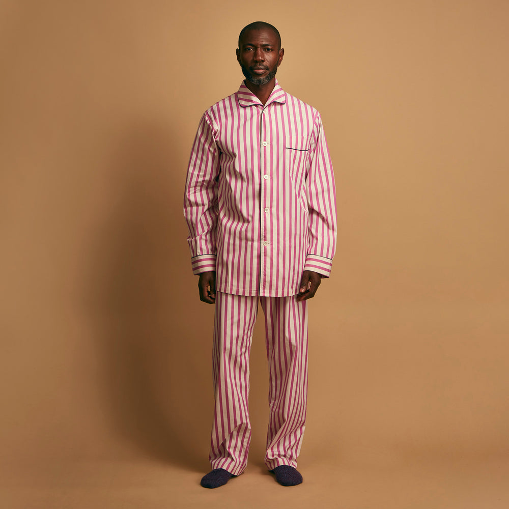The Turnbull & Asser Pink Candy Stripe Cotton Traditional Pyjamas feature long sleeves, pants, vertical pink candy stripes, a camp collar shirt with buttons, chest pocket, and navy trim on the pocket and cuffs.