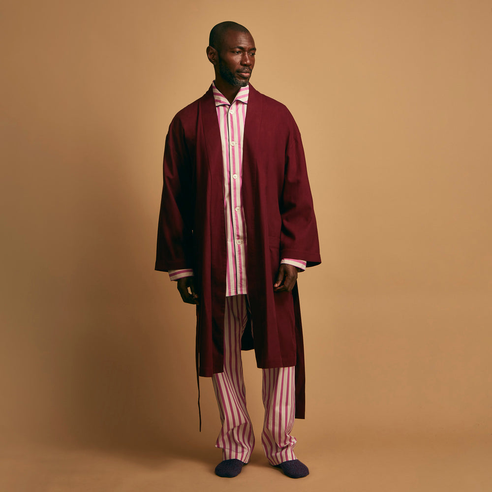 The Turnbull & Asser Pink Candy Stripe Cotton Traditional Pyjamas feature long sleeves, pants, vertical pink candy stripes, a camp collar shirt with buttons, chest pocket, and navy trim on the pocket and cuffs.