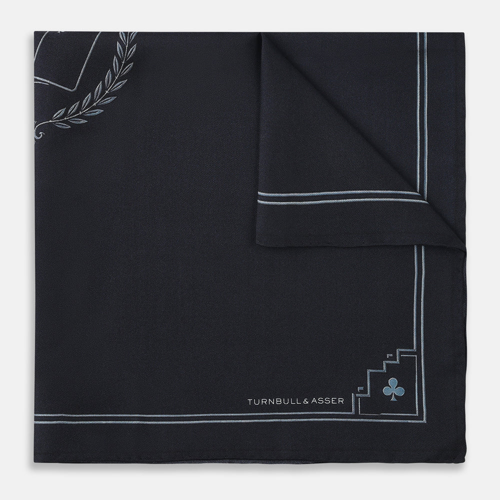 Introducing the Casino Royale Midnight Blue Crest Pocket Square in Silk from Turnbull & Asser UK—a midnight blue silk pocket square bordered in white, featuring playing card suit symbols at each corner and a central motif depicting the 10, J, Q, and K of spades beneath a crown and laurel. Perfect as a sophisticated Casino Royale or Bond tuxedo accessory, with “Turnbull & Asser” elegantly displayed in the lower right.