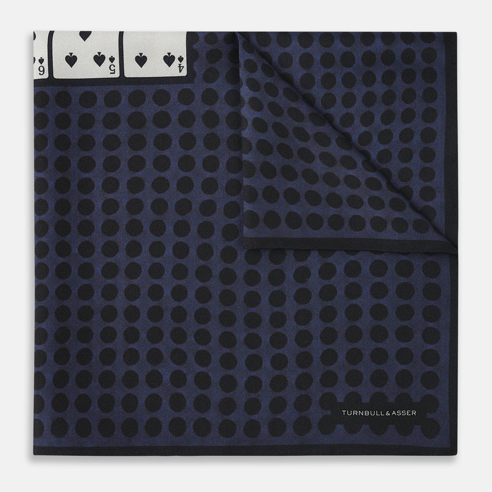 The Casino Royale Midnight Blue Straight Flush Pocket Square in Silk by Turnbull & Asser UK features a rich midnight blue background adorned with a black dotted pattern and showcases five playing cards—the 10, 9, 8, 7, and 6 of spades—arranged in a row at the center for an elegant straight flush design inspired by classic casino style.