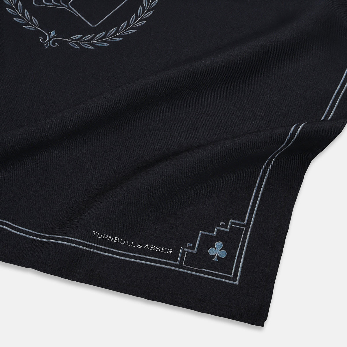 View 2 of product Introducing the Casino Royale Midnight Blue Crest Pocket Square in Silk from Turnbull & Asser UK—a midnight blue silk pocket square bordered in white, featuring playing card suit symbols at each corner and a central motif depicting the 10, J, Q, and K of spades beneath a crown and laurel. Perfect as a sophisticated Casino Royale or Bond tuxedo accessory, with “Turnbull & Asser” elegantly displayed in the lower right.