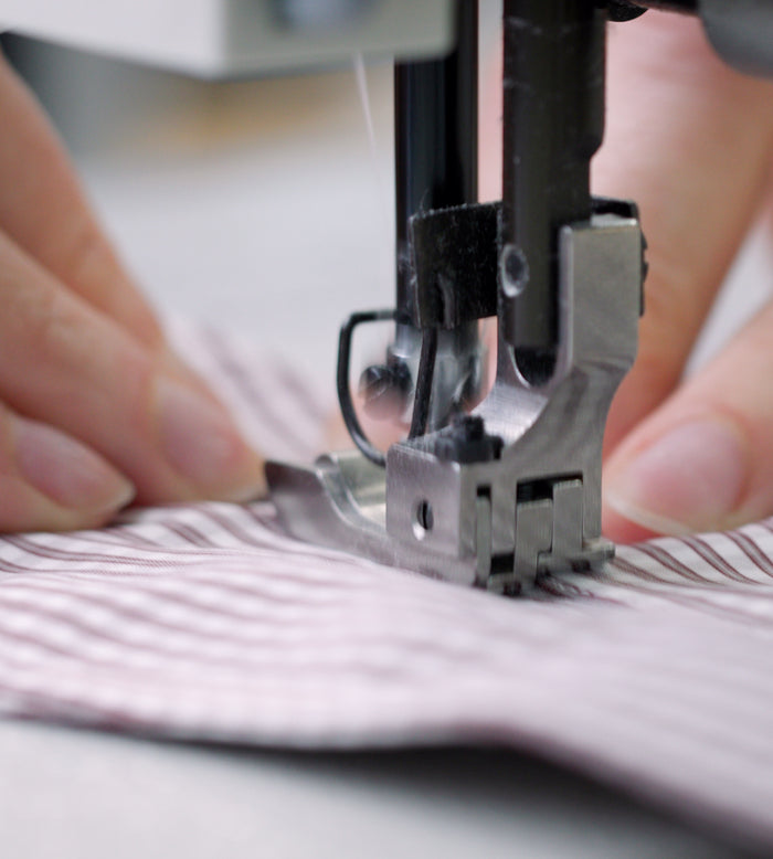 Close-up of hands guiding striped fabric through a sewing machine, with the needle and presser foot in focus as stitching is taking place.
