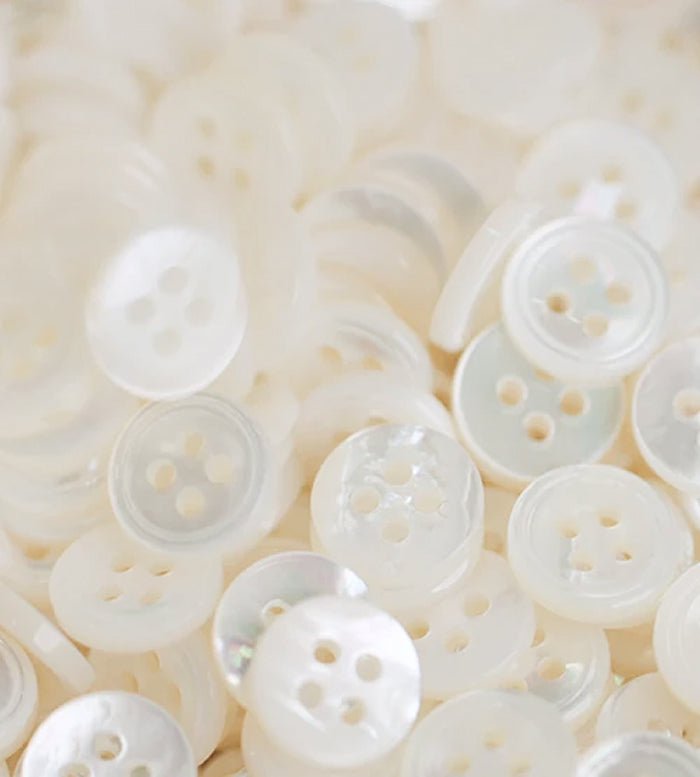 A close-up of a pile of small, round, white buttons with four holes each, featuring a slightly shiny, pearlescent surface.