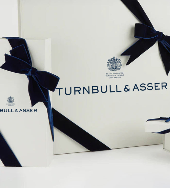 White gift boxes with navy blue velvet ribbons and the Turnbull & Asser logo and crest printed on them, arranged against a white background.