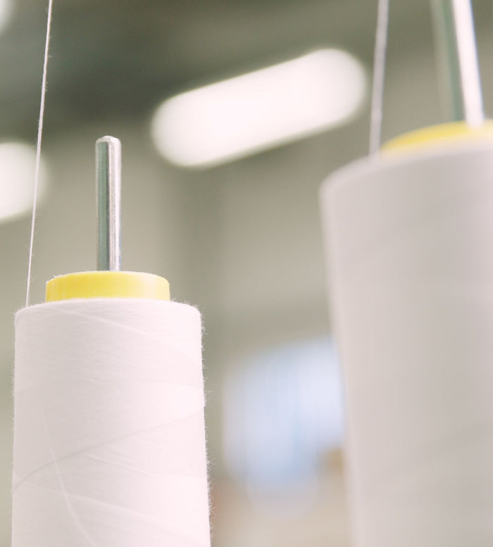 Close-up of two large spools of white thread with metal rods going through their centers, set against a softly blurred background.