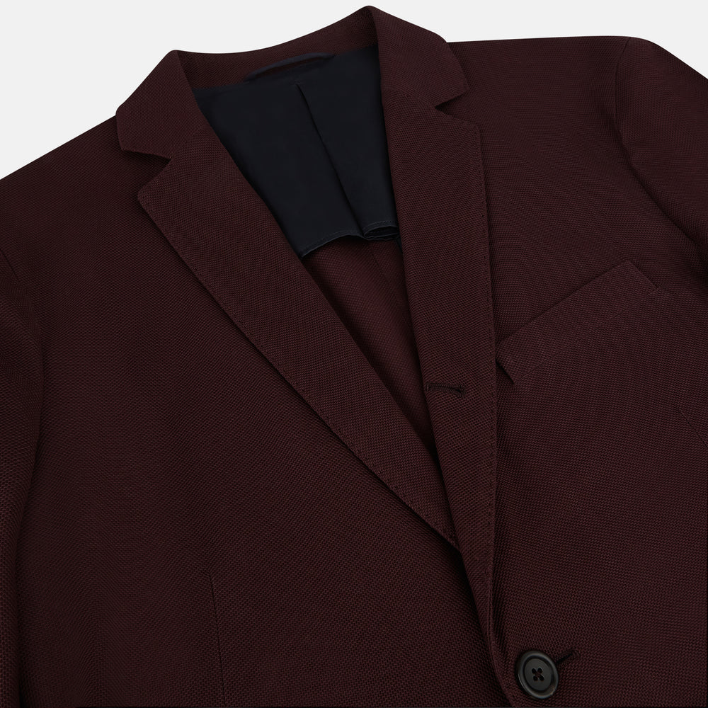 The Turnbull & Asser Burgundy Knitted London Blazer features notch lapels, two front buttons, flap pockets, and a welt chest pocket—ideal for spring and summer—shown against a plain white background.
