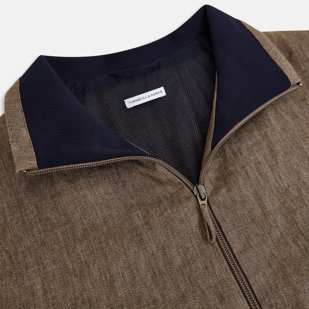 The Fairway Pinecone Golf Jacket in Linen by Turnbull & Asser UK is a brown zip-up jacket featuring a high collar, two side pockets, a zippered chest pocket, and dark cuffs and hem. Crafted from lightweight herringbone linen, it is displayed on a white background.
