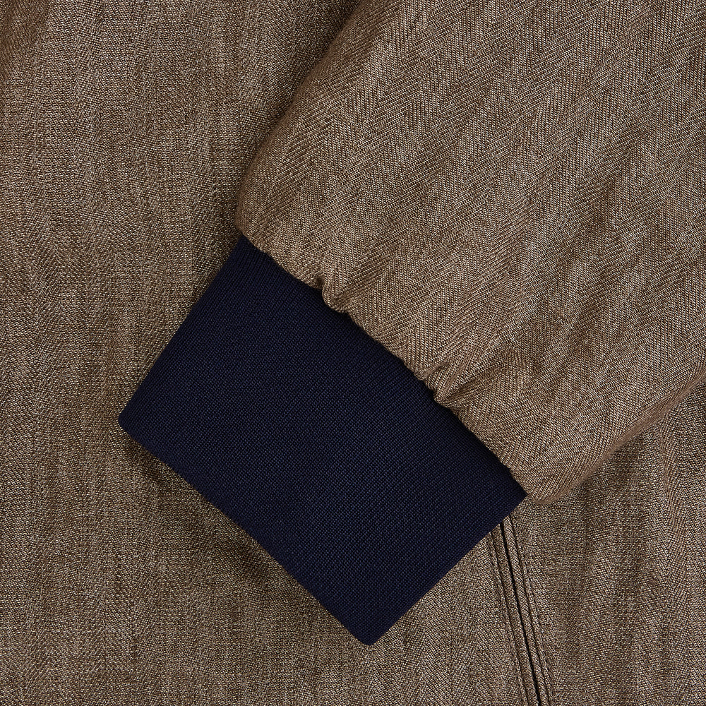The Fairway Pinecone Golf Jacket in Linen by Turnbull & Asser UK is a brown zip-up jacket featuring a high collar, two side pockets, a zippered chest pocket, and dark cuffs and hem. Crafted from lightweight herringbone linen, it is displayed on a white background.
