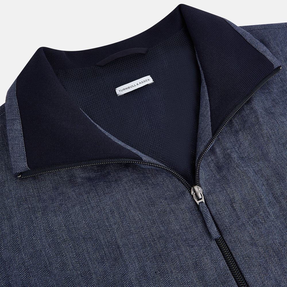 Introducing the Fairway Denim Golf Jacket in Linen by Turnbull & Asser UK—a blue zip-up jacket featuring a high collar, two side pockets, and a zippered chest pocket. The contrasting darker cuffs and hem accentuate its denim-like linen texture, making it the perfect versatile golf jacket for cooler days.