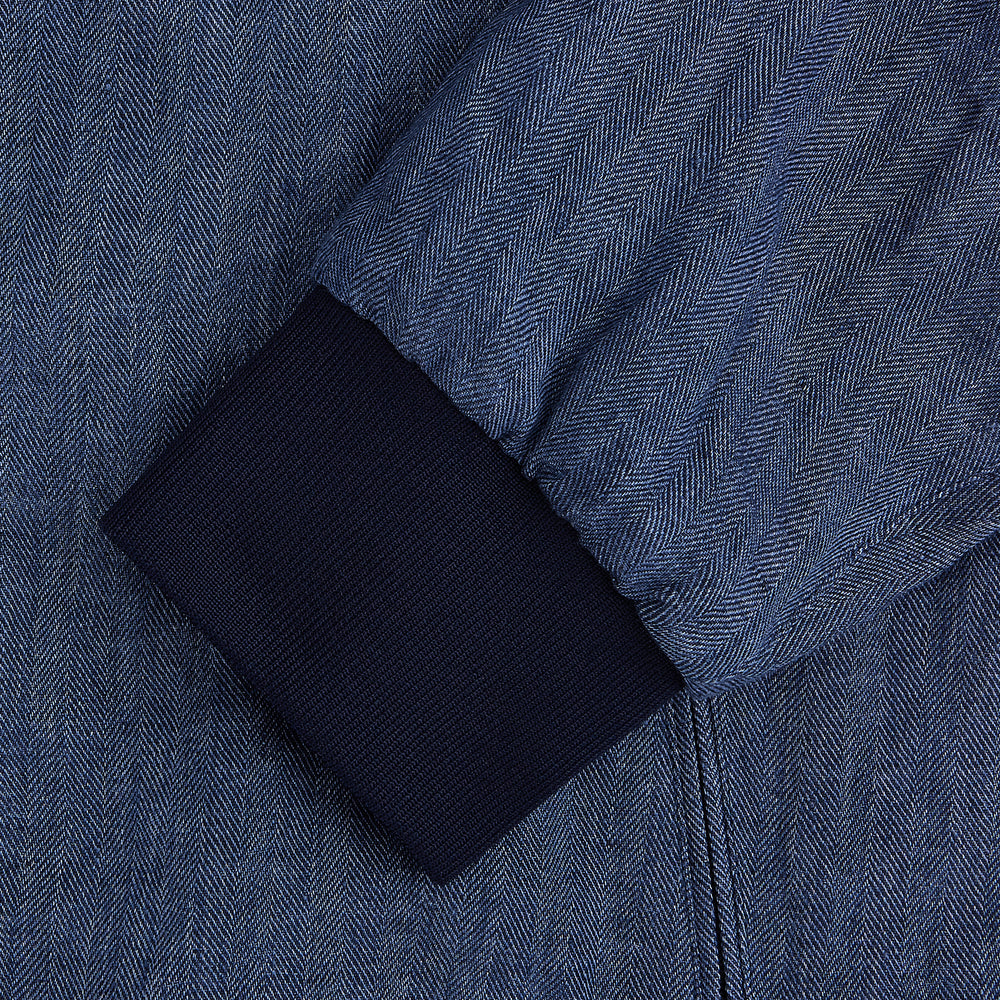 Introducing the Fairway Denim Golf Jacket in Linen by Turnbull & Asser UK—a blue zip-up jacket featuring a high collar, two side pockets, and a zippered chest pocket. The contrasting darker cuffs and hem accentuate its denim-like linen texture, making it the perfect versatile golf jacket for cooler days.