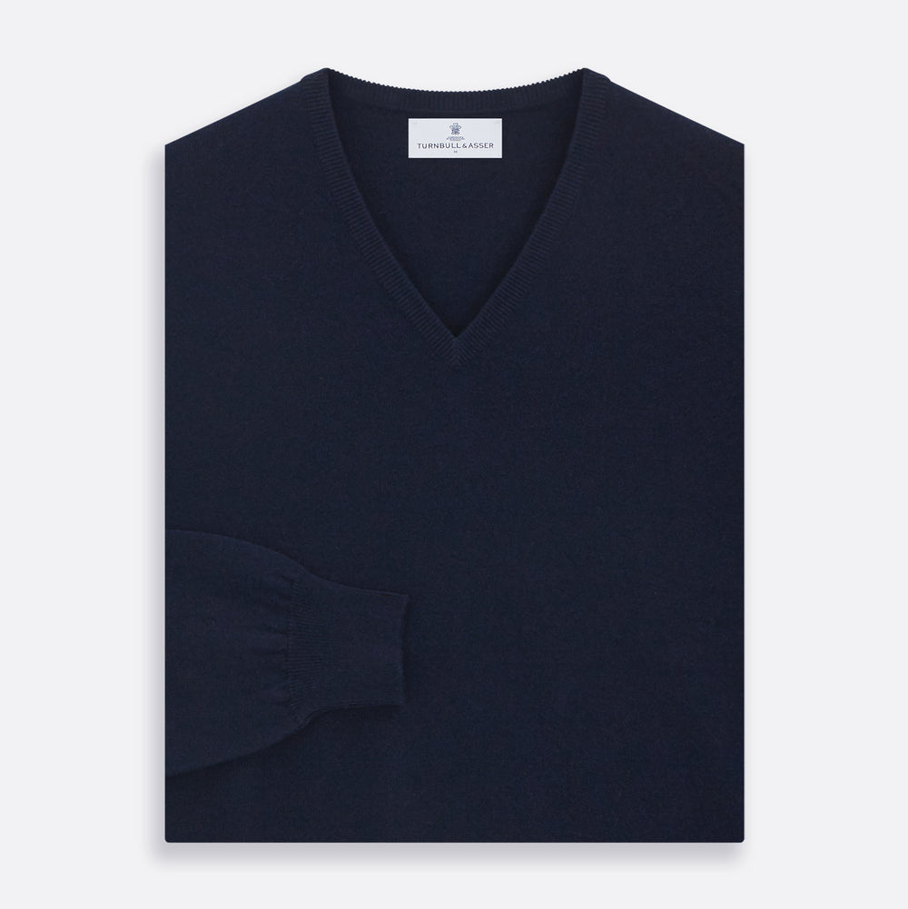 The Turnbull & Asser Navy V-Neck Cashmere Jumper, featuring long sleeves and ribbed cuffs and hem, is laid flat on a white background, showcasing its simple and classic design.