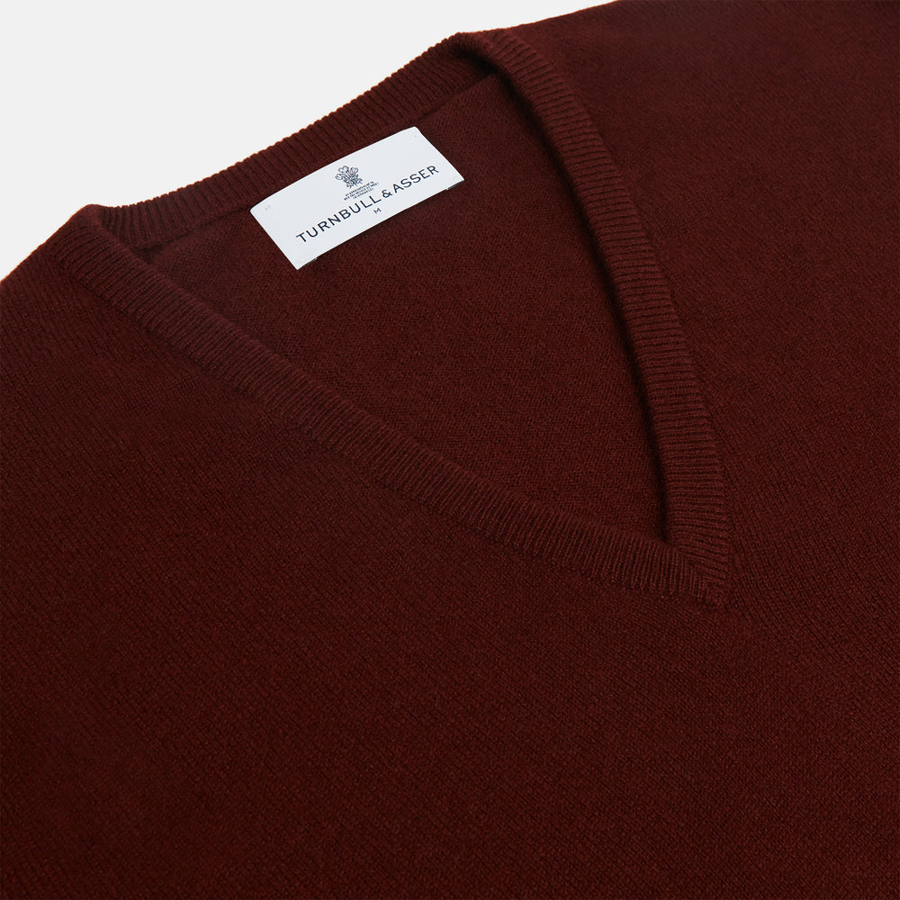 The Turnbull & Asser Port Cashmere V-Neck Jumper is a plain, long-sleeved burgundy sweater with a V-neck, shown flat on a white background.