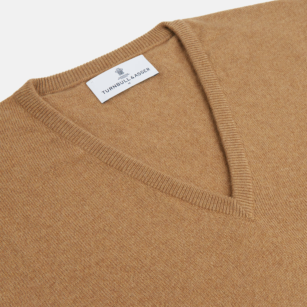 The Turnbull & Asser Natural V-Neck Cashmere Jumper, in camel, features long sleeves and ribbed cuffs, hem, and neckline. Crafted from Scottish cashmere, it’s laid flat on a white background for a refined smart casual look.