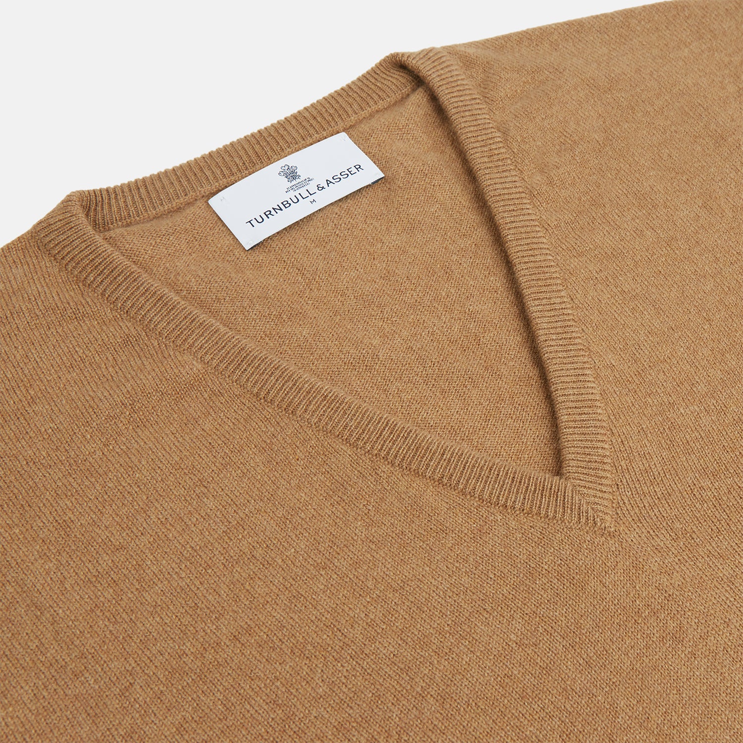 View 2 of product The Turnbull & Asser Natural V-Neck Cashmere Jumper, in camel, features long sleeves and ribbed cuffs, hem, and neckline. Crafted from Scottish cashmere, it’s laid flat on a white background for a refined smart casual look.