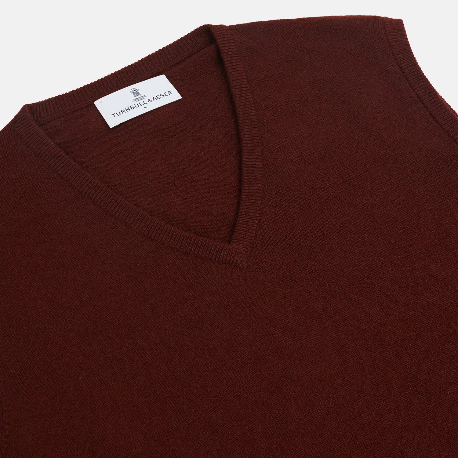 View 2 of product The Turnbull & Asser Port V-Neck Cashmere Slipover is a sleeveless, dark maroon vest with a simple design, shown laid flat on a white background—ideal for layering over a shirt or under a suit jacket.