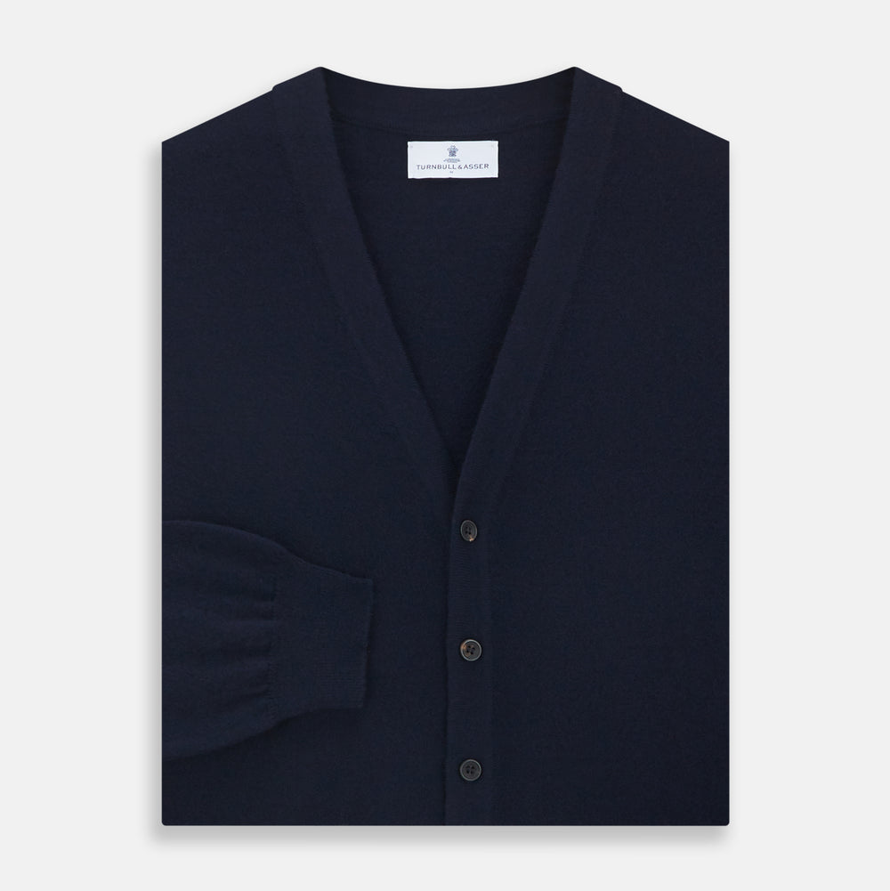 The Navy Cashmere Cardigan by Turnbull & Asser features long sleeves, a V-neckline, button-down front, two front pockets, and ribbed trims, crafted from 21GG cashmere in navy blue and shown laid flat on a white background.