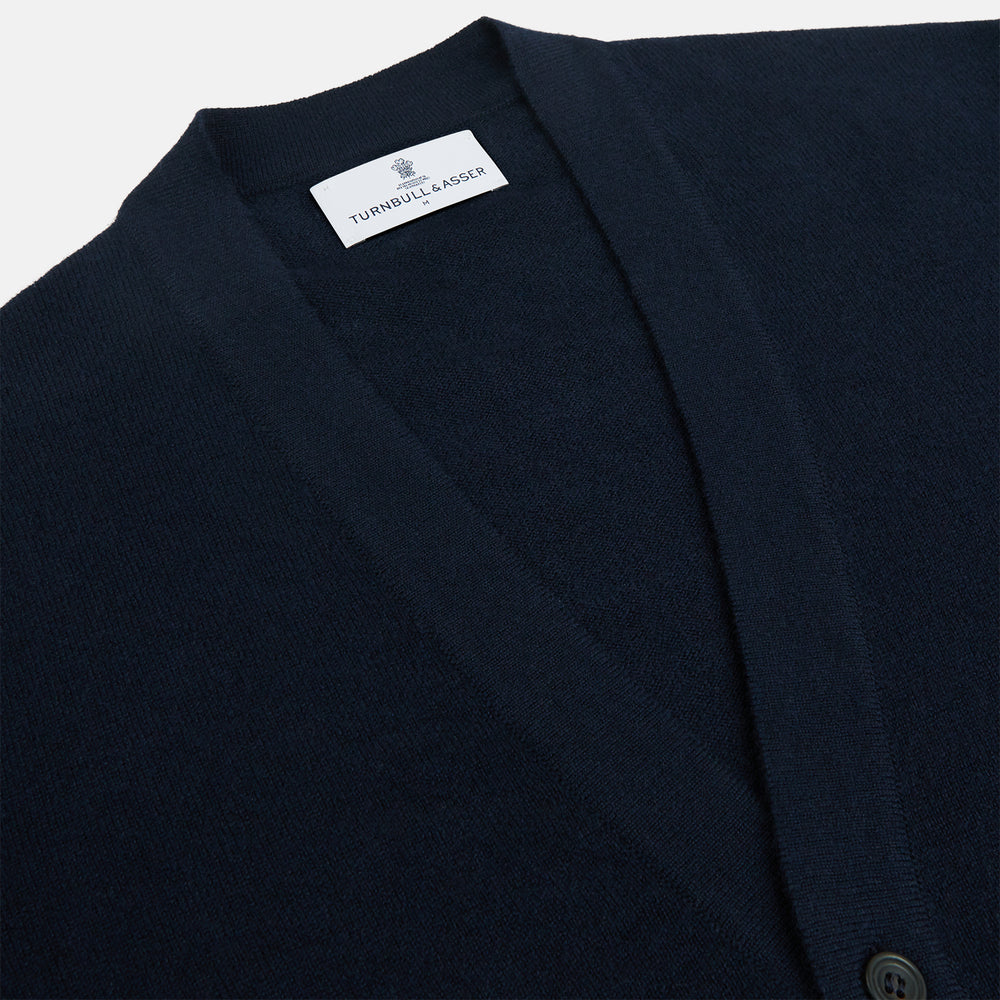The Navy Cashmere Cardigan by Turnbull & Asser features long sleeves, a V-neckline, button-down front, two front pockets, and ribbed trims, crafted from 21GG cashmere in navy blue and shown laid flat on a white background.
